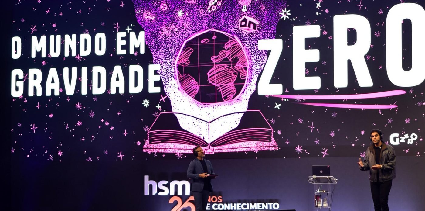 Palco do evento HSM com o telão O mundo em gravidade zero e dois palestrantes.