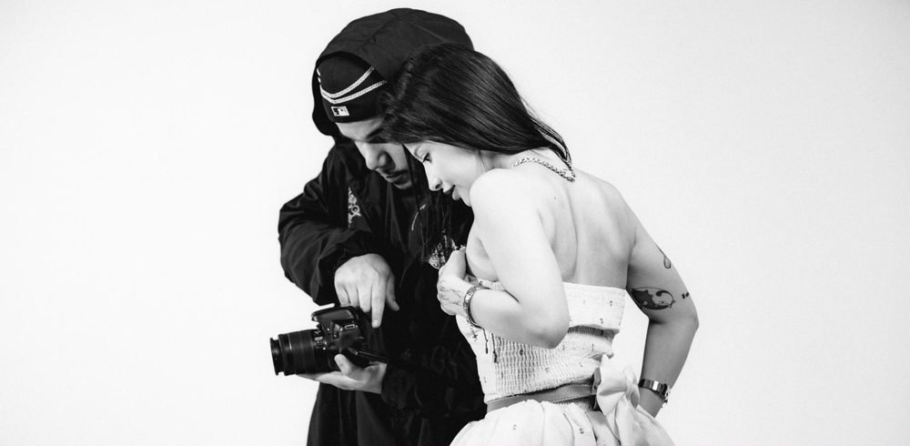 Em preto e branco, fotógrafo mostra a tela da câmera para a modelo durante o ensaio.