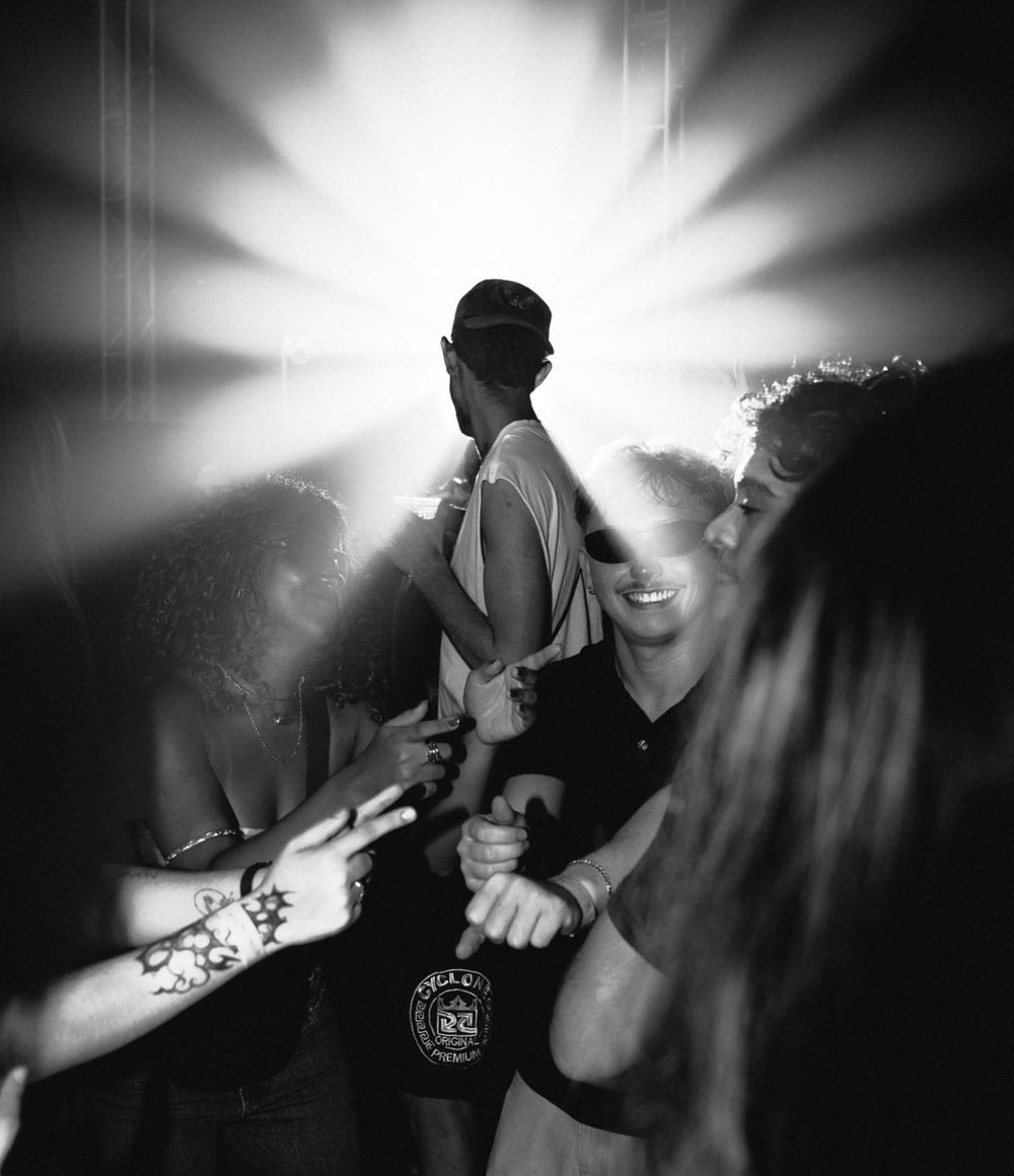 Artista de costas contra o estouro de luz do palco, público com as mãos para o alto.